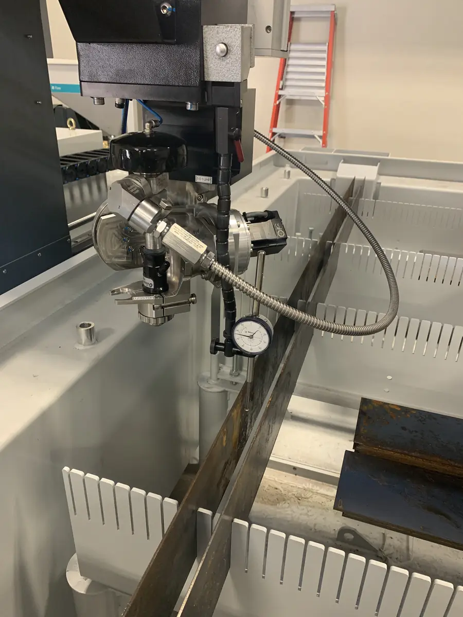 A waterjet cutting head with a Mitutoyo dial indicator mounted against stock, checking alignment over the slat table.