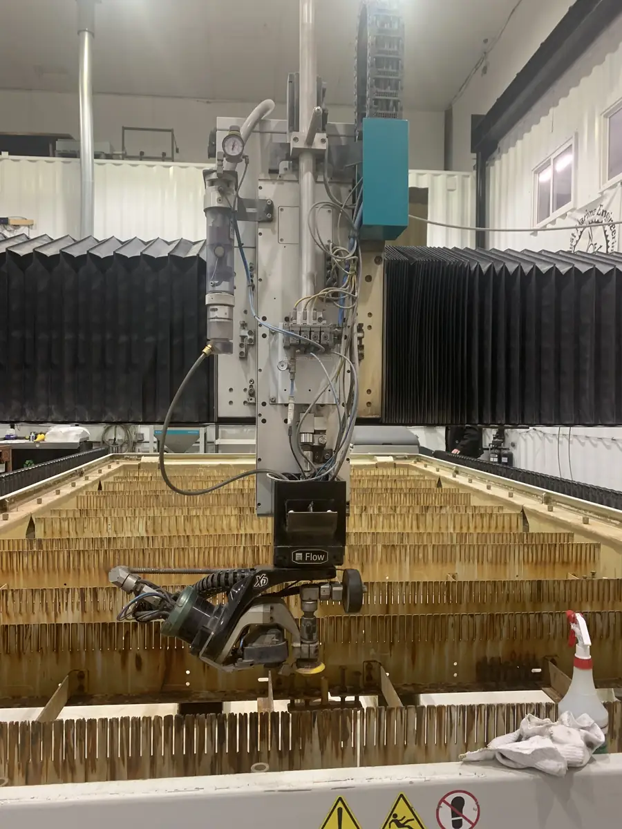 A Flow 5-axis waterjet cutting head over a garnet-stained slat table in a working production shop.